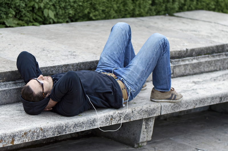 17 - A person reclining on a stone bench, wearing light-wash jeans and a dark hoodie